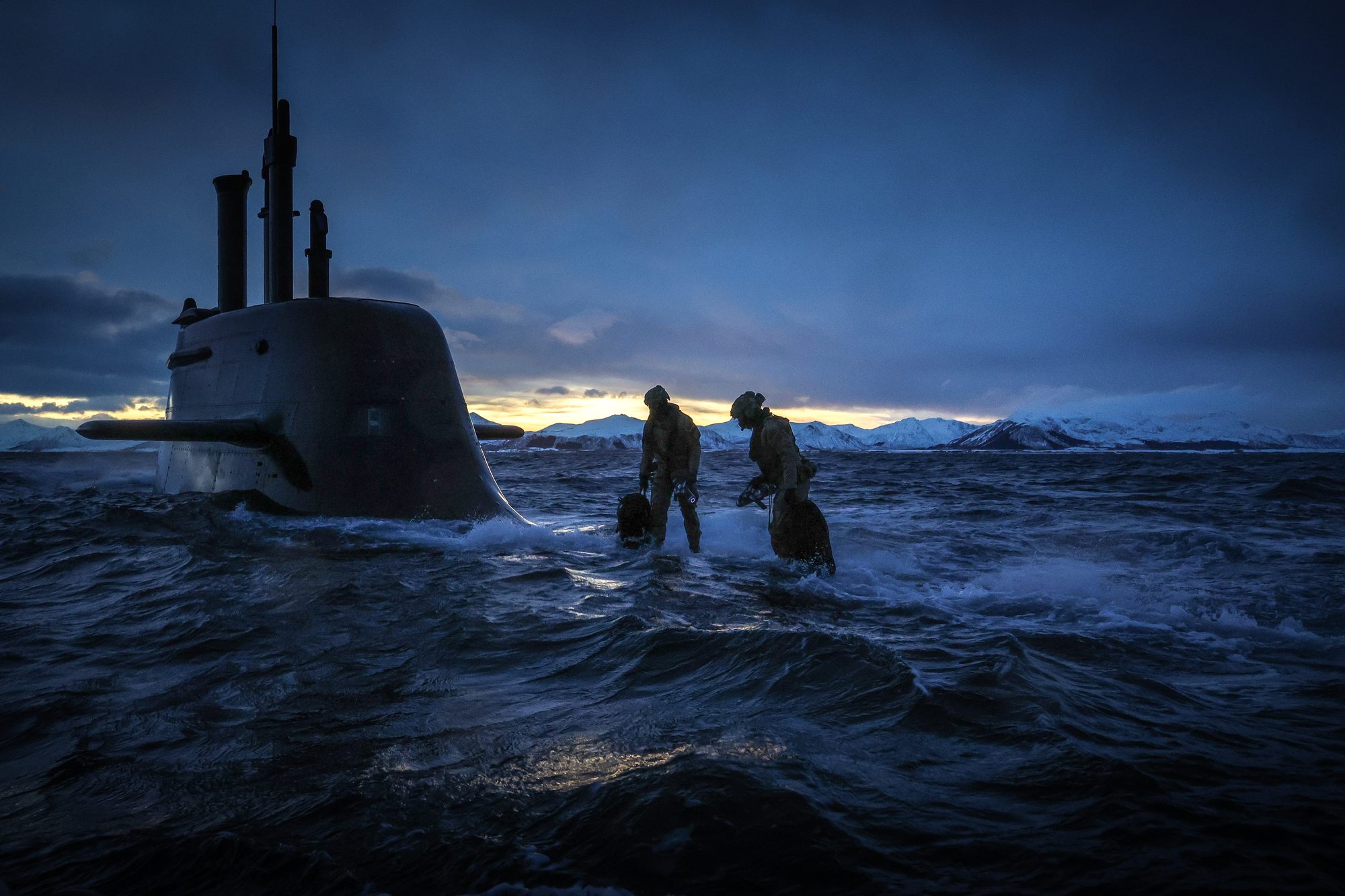 A Royal Navy submarine and personnel at dusk in an Arctic environment.