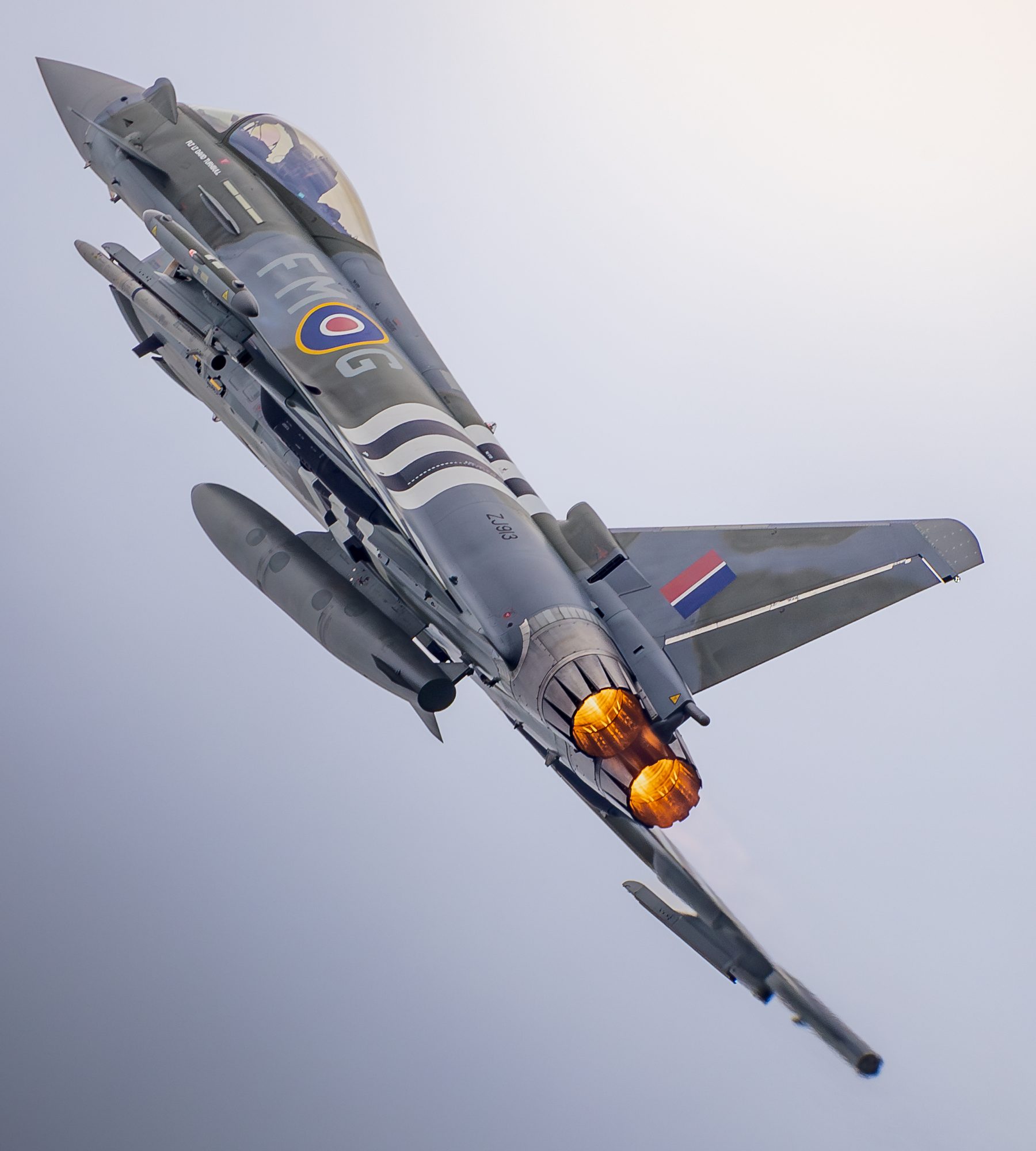 An RAF Typhoon in a steep climbing turn with afterburners lit.