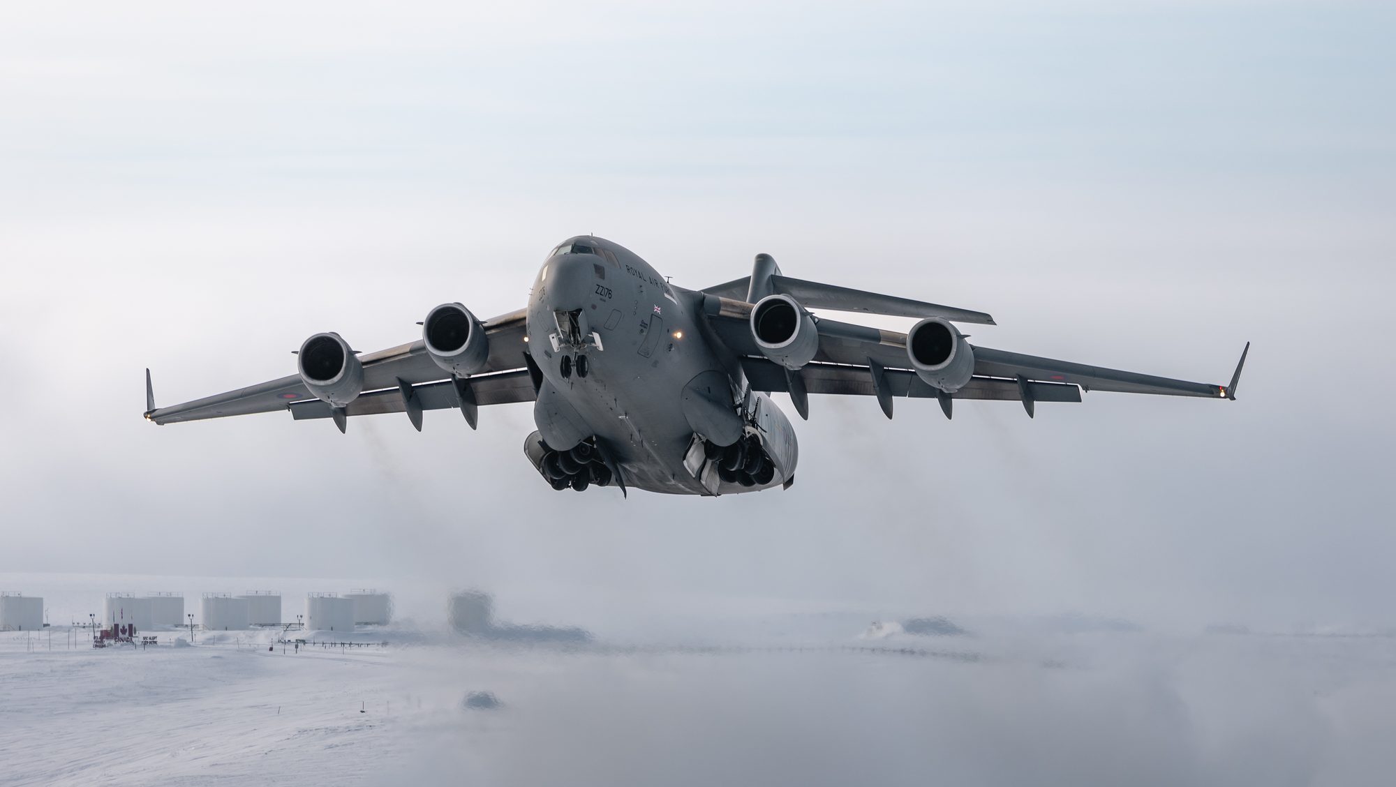An RAF C-17 Globemaster transport aircraft taking off in a snow-covered Arctic environment.