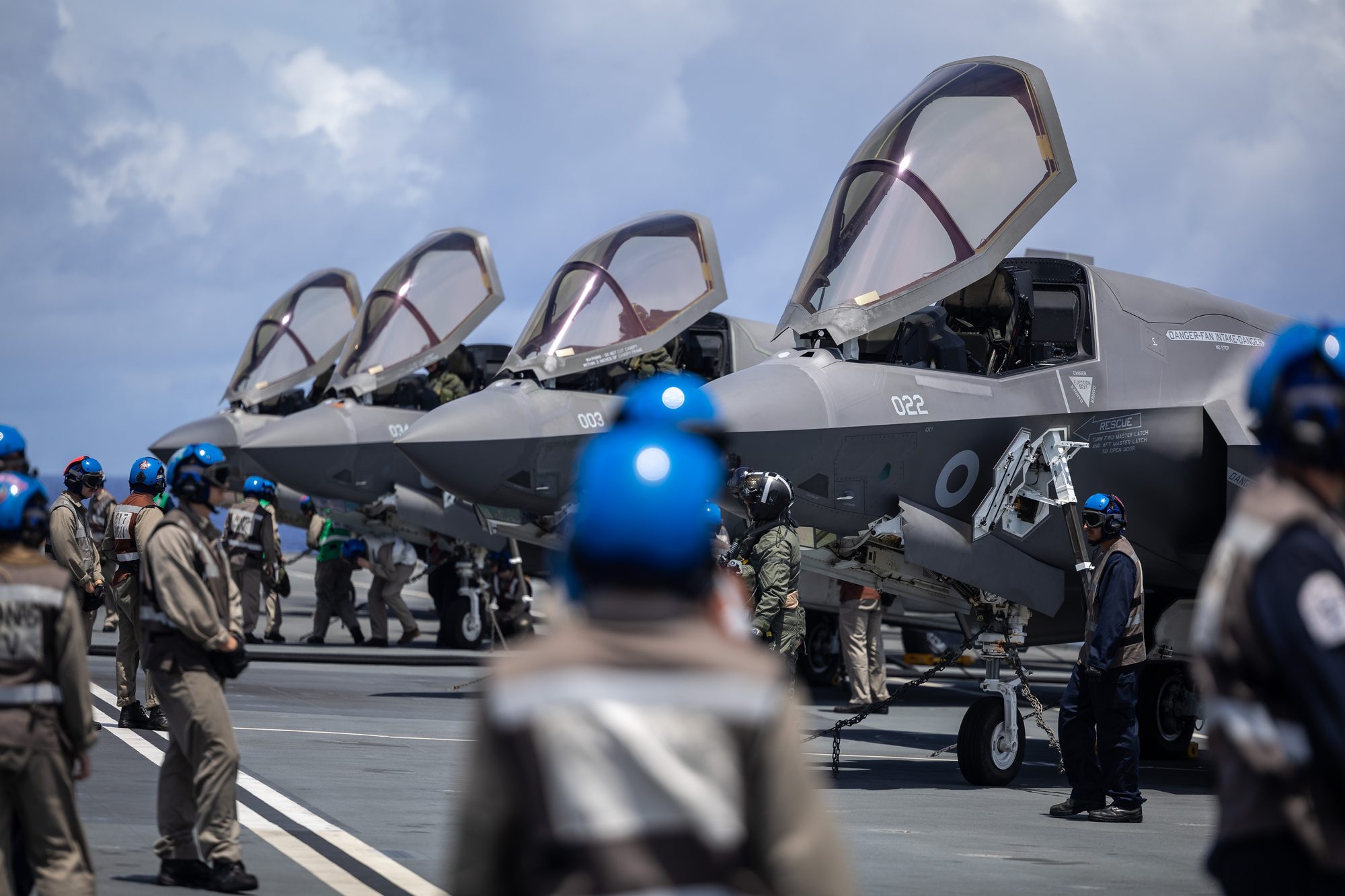 Flight deck crew and technicians preparing F-35 Lightning aircraft aboard a carrier.